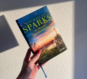 Buch Im Traum bin ich bei dir von Nicholas Sparks vor Wand haltend